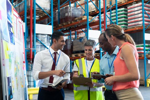 Front view of diverse warehouse staffs discussing over clipboard in warehouse. This is a freight transportation and distribution warehouse. Industrial and industrial workers concept