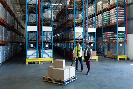 Front view of Caucasian Male staff with his coworker using pallet jack in warehouse. This is a freight transportation and distribution warehouse. Industrial and industrial workers concept