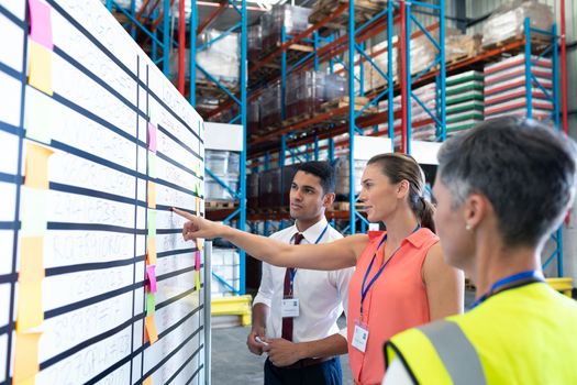Side view of diverse warehouse staffs looking at whiteboard in warehouse. This is a freight transportation and distribution warehouse. Industrial and industrial workers concept