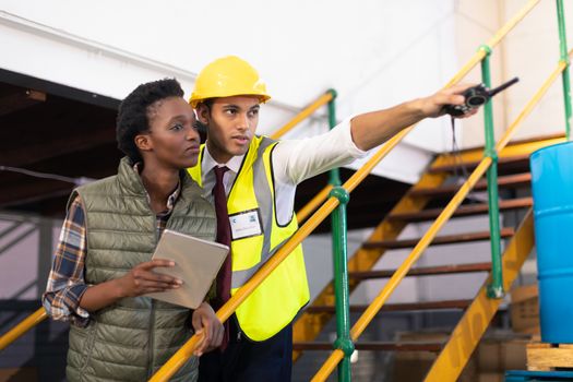 Front view of Caucasian male supervisor with African-american female worker pointing distance in warehouse. This is a freight transportation and distribution warehouse. Industrial and industrial workers concept