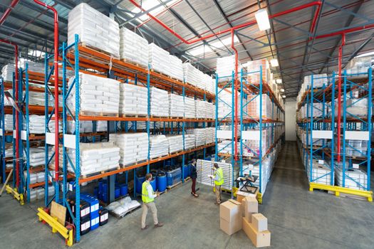 High angle view of mature diverse warehouse staff discussing over whiteboard in warehouse. This is a freight transportation and distribution warehouse. Industrial and industrial workers concept