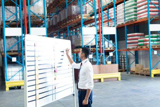 Side view of handsome young Caucasian male staff writing on sticky notes in warehouse. This is a freight transportation and distribution warehouse. Industrial and industrial workers concept