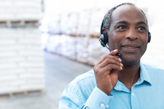 Portrait close-up of handsome mature African-american male supervisor talking on headset in warehouse. This is a freight transportation and distribution warehouse. Industrial and industrial workers concept