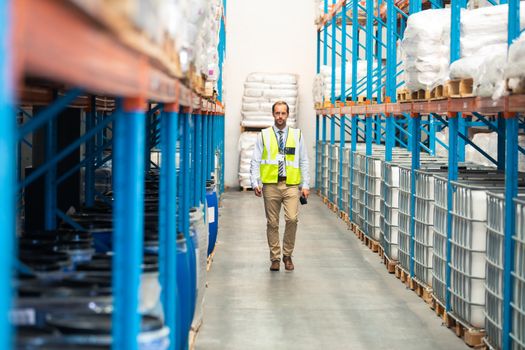 Front view of Caucasian male supervisor walking in aisle of warehouse. This is a freight transportation and distribution warehouse. Industrial and industrial workers concept