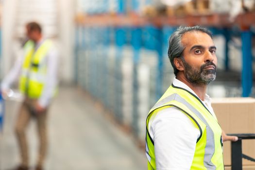 Side view of thoughtful mature Asian male worker looking away in warehouse. This is a freight transportation and distribution warehouse. Industrial and industrial workers concept