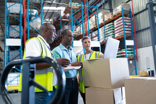 Side view of mature diverse warehouse staffs discussing over laptop in warehouse. This is a freight transportation and distribution warehouse. Industrial and industrial workers concept
