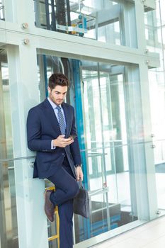 Side view of Young Caucasian businessman looking at mobile phone while standing in modern office