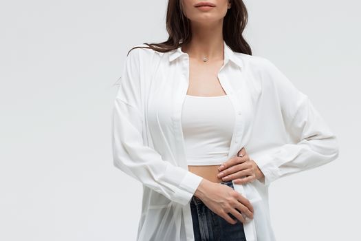 Crop confident long haired woman in white shirt and lingerie and jeans with crossed hands on white background