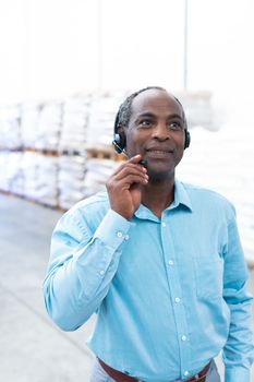 Portrait close-up of handsome mature African-american male supervisor talking on headset in warehouse. This is a freight transportation and distribution warehouse. Industrial and industrial workers concept