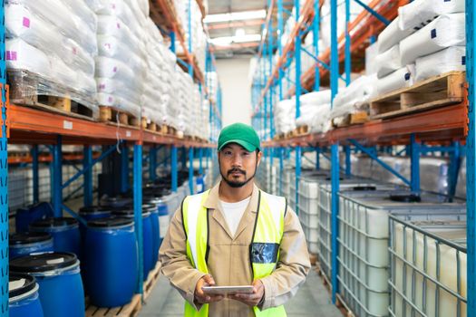 Front view of handsome mature Asian male worker looking at camera while working in warehouse. This is a freight transportation and distribution warehouse. Industrial and industrial workers concept