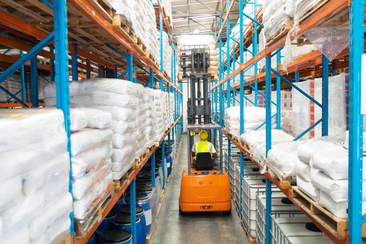 Rear view of mature African-american male worker driving forklift in warehouse. This is a freight transportation and distribution warehouse. Industrial and industrial workers concept
