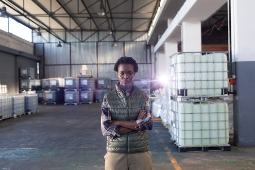 Front view of African-american female staff standing with arms crossed in warehouse. This is a freight transportation and distribution warehouse. Industrial and industrial workers concept