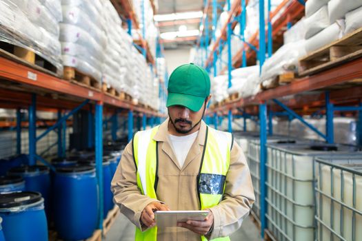 Front view of handsome mature Asian male worker checking stocks on digital tablet in warehouse. This is a freight transportation and distribution warehouse. Industrial and industrial workers concept