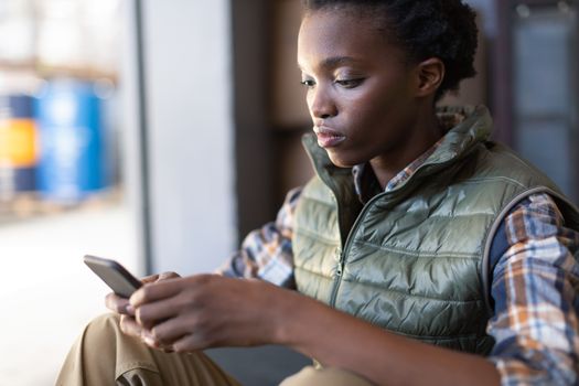 Side view of African-american female worker using mobile phone in warehouse. This is a freight transportation and distribution warehouse. Industrial and industrial workers concept