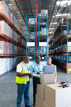 Front view of mature diverse warehouse staffs discussing over laptop in warehouse. This is a freight transportation and distribution warehouse. Industrial and industrial workers concept