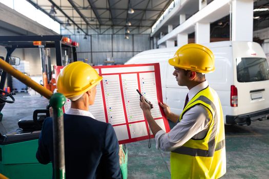 Rear view of Caucasian female manager and Caucasian male supervisor discussing over inventory chart in warehouse. This is a freight transportation and distribution warehouse. Industrial and industrial workers concept