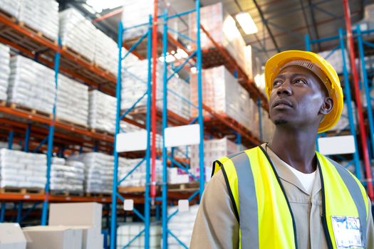 Close-up of thoughtful African-american male worker looking away in warehouse. This is a freight transportation and distribution warehouse. Industrial and industrial workers concept