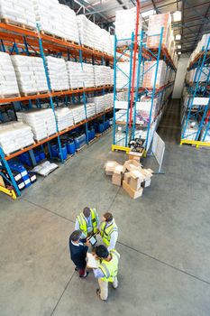 High angle view of diverse warehouse staff discussing over digital tablet in warehouse. This is a freight transportation and distribution warehouse. Industrial and industrial workers concept