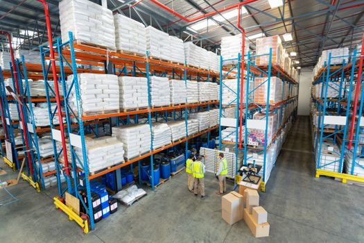 High angle view of mature diverse warehouse staff discussing over whiteboard in warehouse. This is a freight transportation and distribution warehouse. Industrial and industrial workers concept