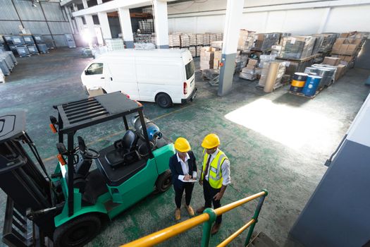 High angle view of Caucasian female manager and male supervisor discussing over clipboard in warehouse. This is a freight transportation and distribution warehouse. Industrial and industrial workers concept