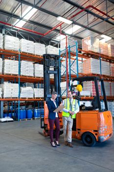 Front view of mature Caucasian male and female staff working together near forklift in warehouse. This is a freight transportation and distribution warehouse. Industrial and industrial workers concept