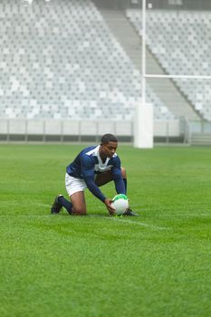 Front view of African American male rugby player placing rugby ball on the stand in stadium