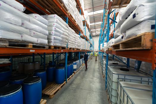 Side view of diverse warehouse staff checking stocks in aisle in warehouse. They are holding clipboards and writing in it. This is a freight transportation and distribution warehouse. Industrial and industrial workers concept