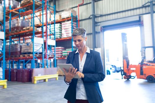 Front view of pretty mature Caucasian female manager using digital tablet in warehouse. This is a freight transportation and distribution warehouse. Industrial and industrial workers concept