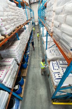 High angle of diverse warehouse staff checking stocks in aisle in warehouse. They are holding clipboards and writing in it. This is a freight transportation and distribution warehouse. Industrial and industrial workers concept