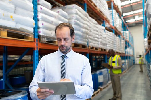 Front view of mature Caucasian male supervisor working on digital tablet in warehouse. This is a freight transportation and distribution warehouse. Industrial and industrial workers concept