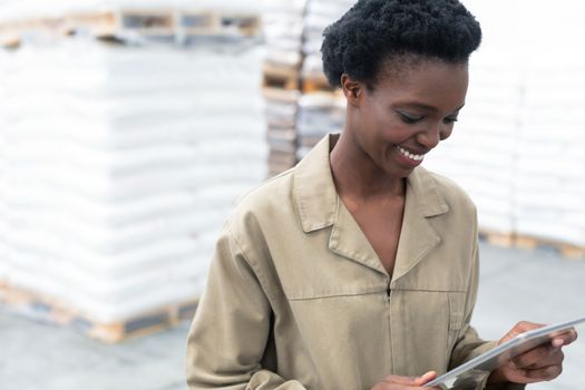 Close-up of beautiful young African-american female worker working on digital tablet in warehouse. This is a freight transportation and distribution warehouse. Industrial and industrial workers concept