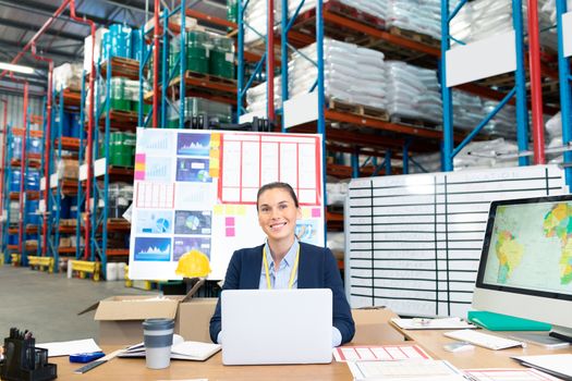 Portrait of beautiful young Caucasian female manager using laptop at desk in warehouse. This is a freight transportation and distribution warehouse. Industrial and industrial workers concept