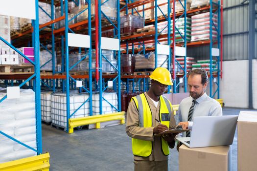 Front view of diverse staffs discussing over clipboard in warehouse. This is a freight transportation and distribution warehouse. Industrial and industrial workers concept