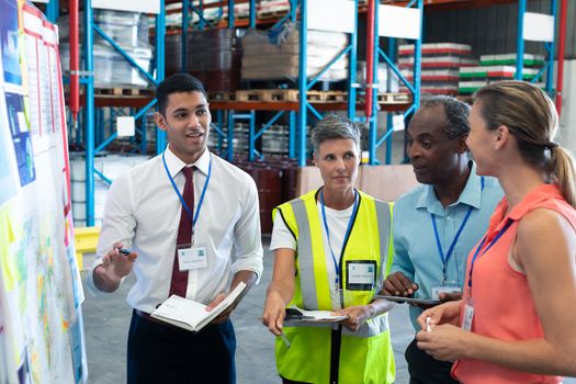 Front view of diverse warehouse staffs discussing over whiteboard in warehouse. This is a freight transportation and distribution warehouse. Industrial and industrial workers concept