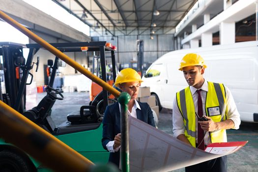 Front view of Caucasian female manager and Caucasian male supervisor discussing over inventory chart in warehouse. This is a freight transportation and distribution warehouse. Industrial and industrial workers concept
