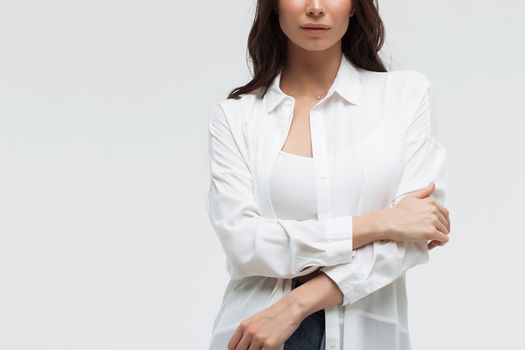 Crop confident long haired woman in white shirt and lingerie and jeans with crossed hands on white background