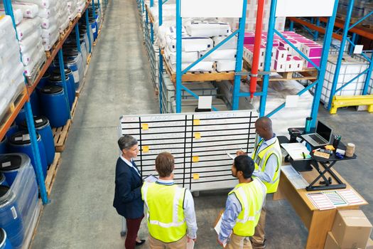 High angle view of diverse warehouse staff discussing over whiteboard in warehouse. This is a freight transportation and distribution warehouse. Industrial and industrial workers concept