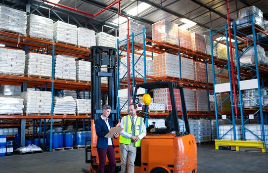 Front view of mature Caucasian male and female staff working together near forklift in warehouse. This is a freight transportation and distribution warehouse. Industrial and industrial workers concept