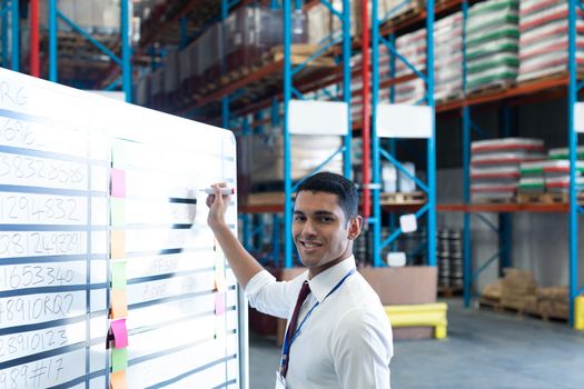 Portrait of handsome young Caucasian male supervisor writing on whiteboard in warehouse. This is a freight transportation and distribution warehouse. Industrial and industrial workers concept