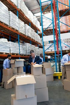 Front view of mature diverse staff unpacking cardboard boxes in warehouse. This is a freight transportation and distribution warehouse. Industrial and industrial workers concept