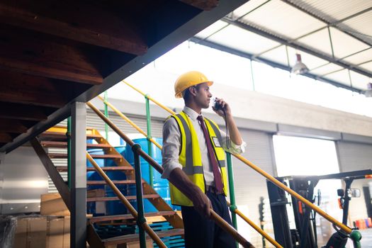 Side view of Caucasian Male supervisor talking on talkie walkie on stairs in warehouse. This is a freight transportation and distribution warehouse. Industrial and industrial workers concept