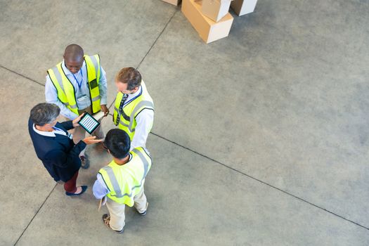 High angle view of diverse warehouse staff discussing over digital tablet in warehouse. This is a freight transportation and distribution warehouse. Industrial and industrial workers concept