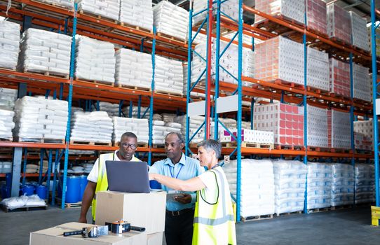 Front view of mature diverse warehouse staffs discussing over laptop in warehouse. This is a freight transportation and distribution warehouse. Industrial and industrial workers concept