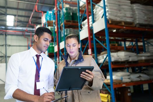 Front view of diverse staffs discussing over digital tablet in warehouse. This is a freight transportation and distribution warehouse. Industrial and industrial workers concept