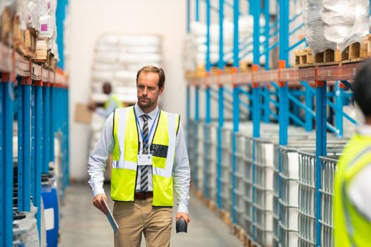 Front view of handsome mature Caucasian male supervisor walking in warehouse. This is a freight transportation and distribution warehouse. Industrial and industrial workers concept