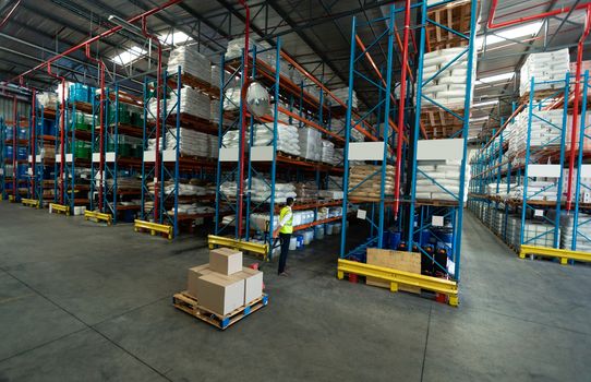 Rear view of Young Caucasian male staff using pallet jack in warehouse. This is a freight transportation and distribution warehouse. Industrial and industrial workers concept