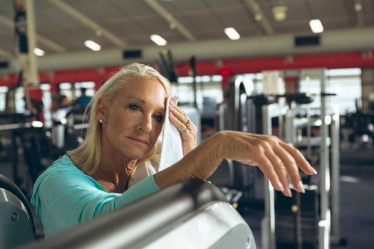 Front view of tired active senior Caucasian woman wiping sweat towel in fitness studio. Strong active senior female amputee training and working out