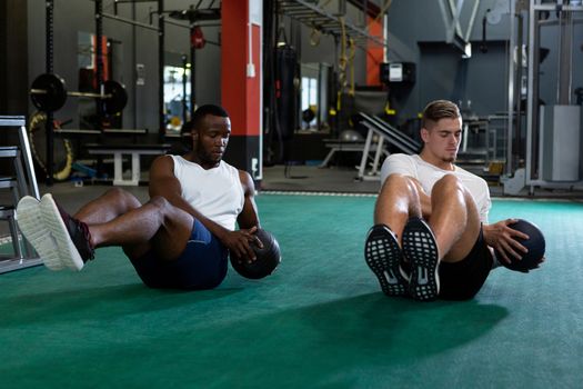 Front view of handsome young diverse male athletics exercising together with exercise ball in fitness center. Bright modern gym with fit healthy people working out and training