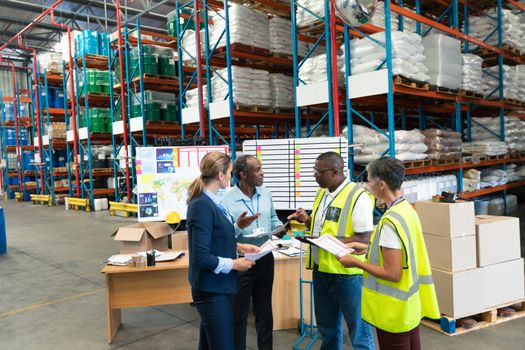 Front view of mature diverse staffs discussing over document in warehouse. This is a freight transportation and distribution warehouse. Industrial and industrial workers concept