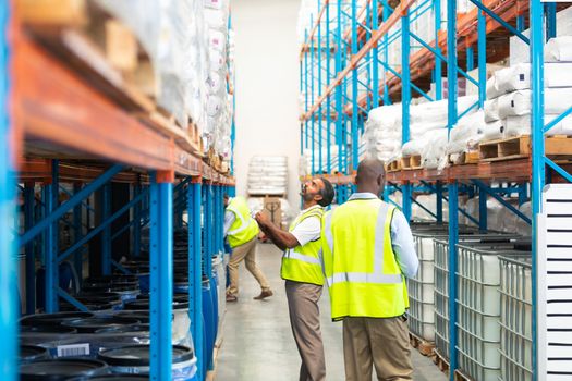 Side view of attentive mature diverse male workers in yellow vests checking stocks in warehouse. This is a freight transportation and distribution warehouse. Industrial and industrial workers concept